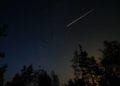 Night scene with starry sky and meteorite trail over forest. Long exposure shoot