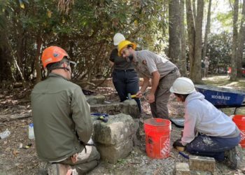 Four park employees encircle large stones with mallets and a bucket of mortar.