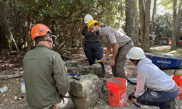 Four park employees encircle large stones with mallets and a bucket of mortar.