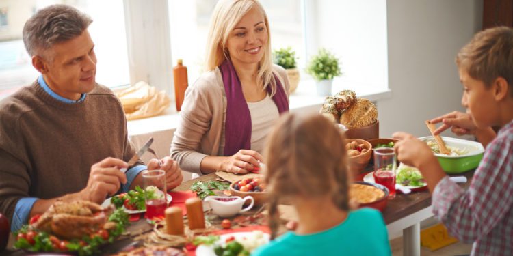 Happy family of four eating traditional Thanksgiving food by the table; Shutterstock ID 225143896; PO: HomeLife1124