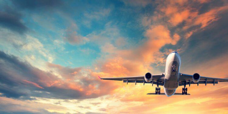 Landing airplane. Landscape with white passenger airplane is flying in the blue sky with multicolored clouds at sunset. Travel background. Passenger airliner. Business trip. Commercial aircraft