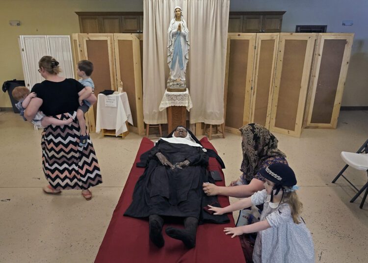 People pray over the body of Sister Wilhelmina Lancaster at the Benedictines of Mary, Queen of Apostles abbey Sunday, May 28, 2023, near Gower, Mo. Hundreds of people visited the small town in Missouri this week to see the nun's body that has barely decomposed since 2019 — some are saying it's a sign of holiness in Catholicism, while others are saying the lack of decomposition may not be as rare as people think.  (AP Photo/Charlie Riedel)