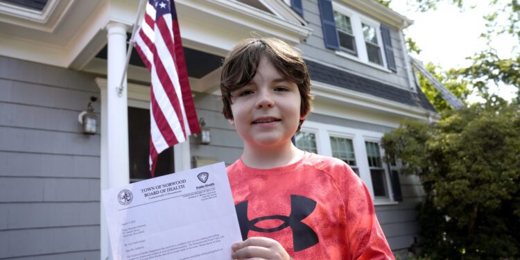 Danny Doherty, 12, of Norwood, Mass., stands for a photograph Wednesday, Aug. 21, 2024, in front of his home in Norwood, while holding a letter from the Town of Norwood Board of Health advising his family that they may not sell homemade ice cream at an ice cream stand near their home. (AP Photo/Steven Senne)